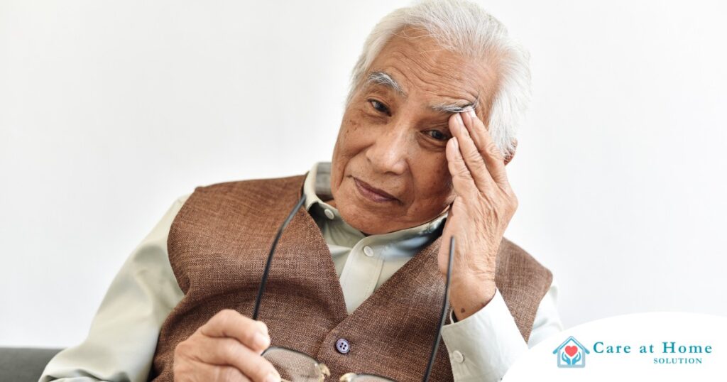 An older adult holds his head and his glasses representing vision problems like macular degeneration.