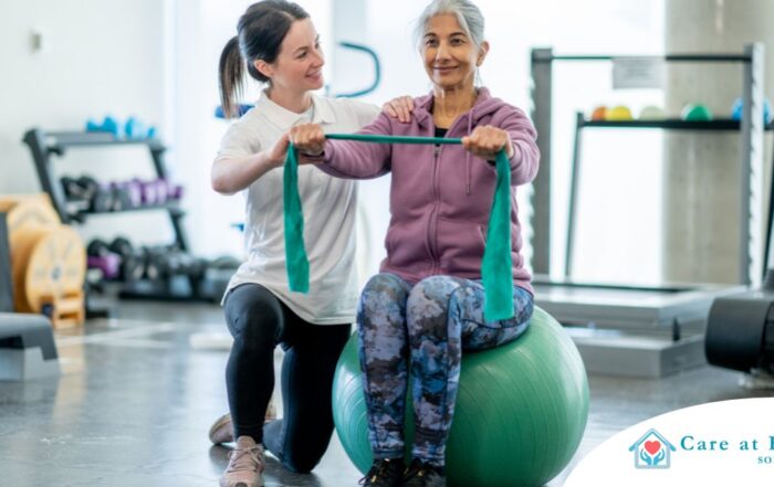 A care provider helps an older woman exercise with a resistance band and an exercise ball, representing how exercise can help with senior fall prevention.